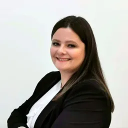 Portret uśmiechniętej kobiety w czarnej marynarce i białej bluzce na jasnym tle, sugerujący profesjonalizm w branży finansowej.