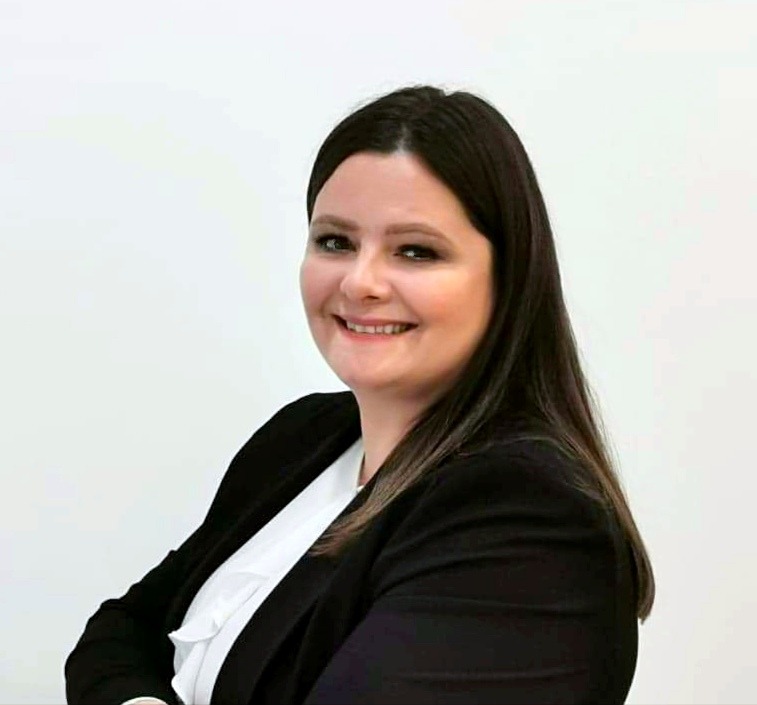 Portret uśmiechniętej kobiety w czarnej marynarce i białej bluzce na jasnym tle, sugerujący profesjonalizm w branży finansowej.