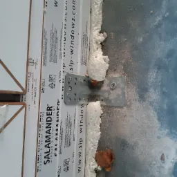 Detail montażu okna PCV z widoczną pianką montażową, metalowym mocowaniem i folią ochronną Salamander.