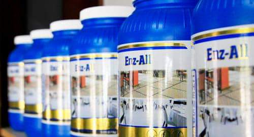 Rząd niebieskich butelek środka czyszczącego Enz-All z ilustracjami czystych wnętrz na etykietach, sugerujących zastosowanie do sprzątania powierzchni.