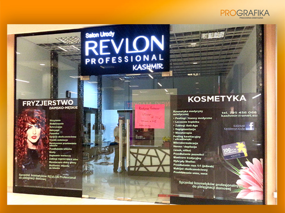 Witryna salonu urody Revlon Professional Kashmir z reklamami fryzjerstwa damsko-męskiego i kosmetyki medycznej, widoczne menu usług i logo firmy Prografika w prawym górnym rogu.