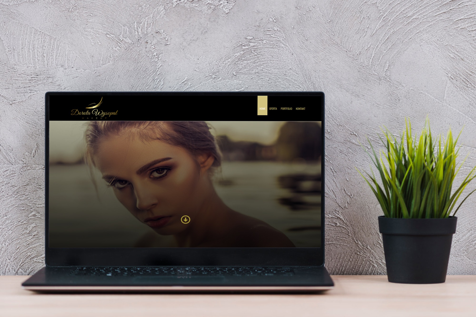 Laptop wyświetlający stronę internetową Doroty Wysopal MakeUp, z widocznym logo i zdjęciem modelki, na biurku obok doniczki z zieloną rośliną, na tle szarej ściany o teksturowanej powierzchni.
