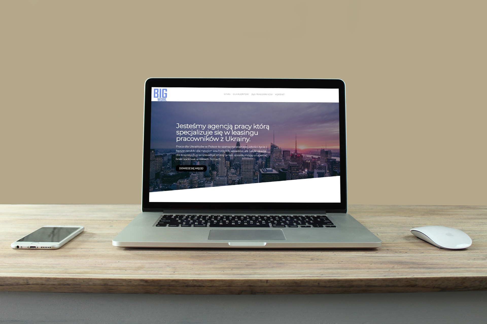 Laptop wyświetlający stronę internetową agencji pracy Big Work na drewnianym biurku, obok smartfon i myszka.