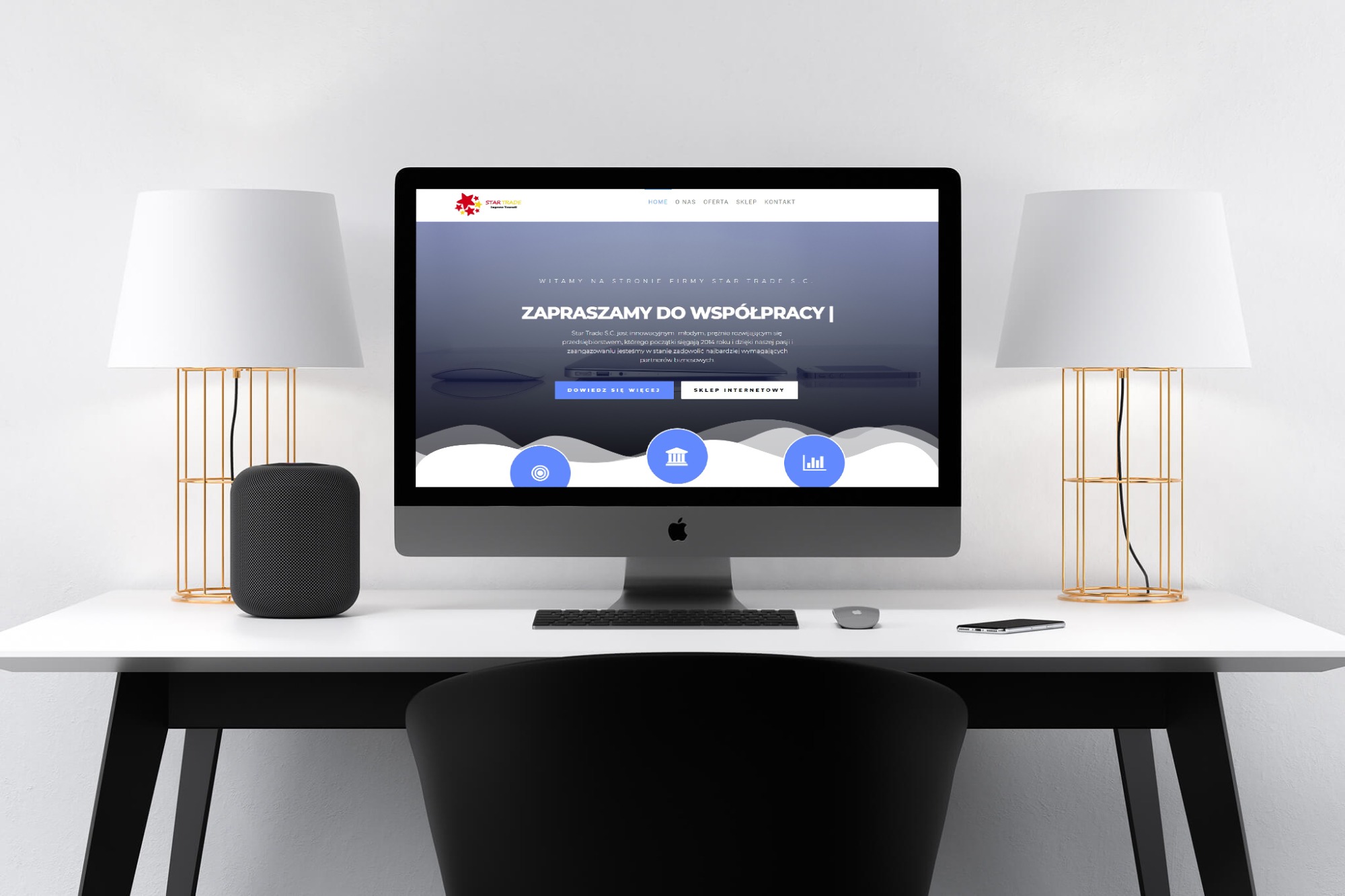 Ekran komputera iMac prezentujący stronę internetową StarTrade z hasłem 'Zapraszamy do współpracy', na białym biurku z lampami i głośnikiem, widok zza czarnego krzesła.