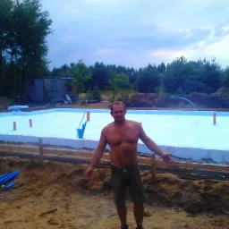 Fundamenty domu jednorodzinnego: izolacja z niebieskiego styropianu, szalunek i zbrojenie. Mężczyzna pozuje na tle prac.