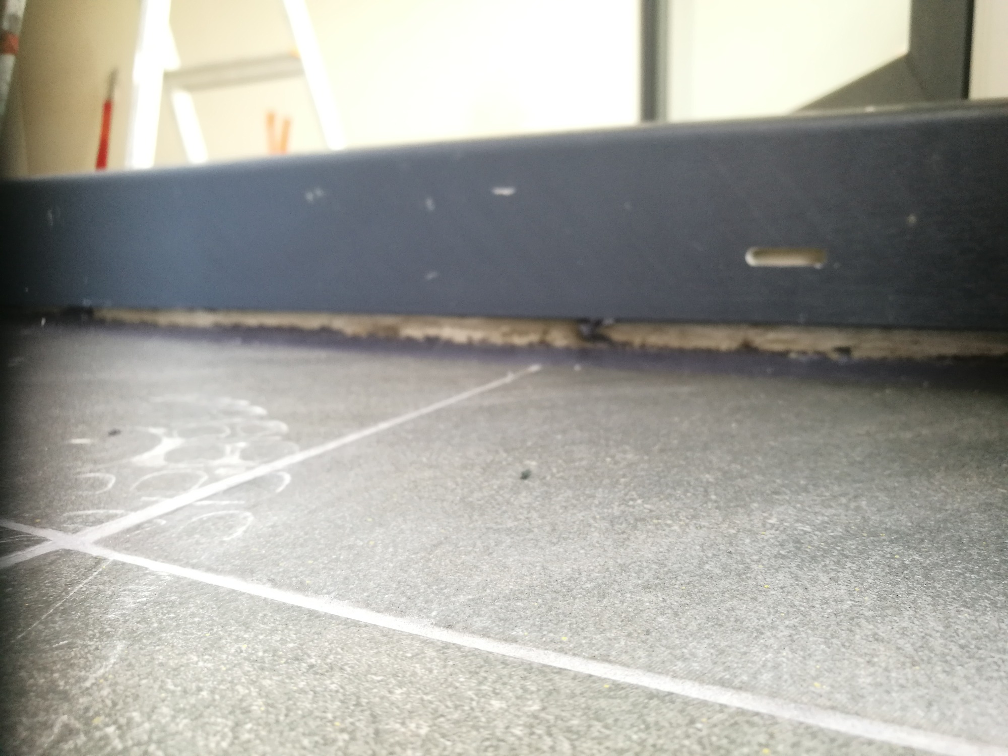 Szare płytki podłogowe z fugami, widoczna listwa przypodłogowa i ślady po czyszczeniu