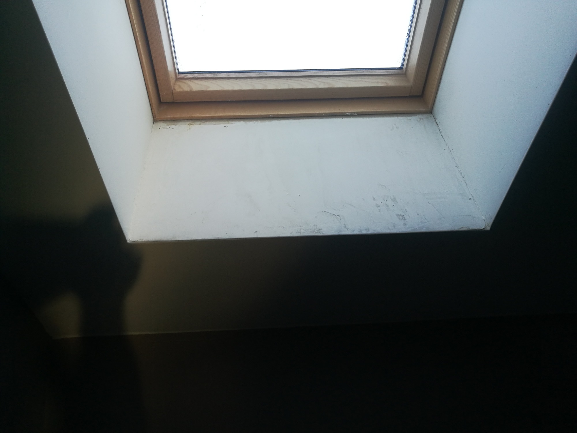 Montaż okna dachowego z drewnianą ramą i wykończeniem gipsowym, widoczne niedoskonałości w szpachlowaniu.