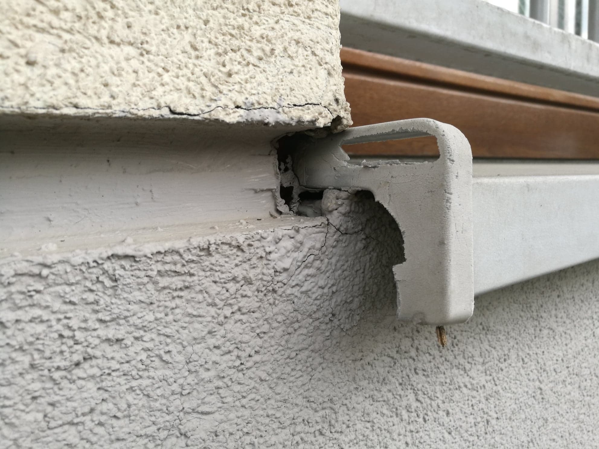 Pęknięcia i uszkodzenia tynku na elewacji budynku przy oknie, widoczne odpryski farby i naruszona struktura.