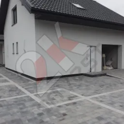 Nowoczesny dom z szarą kostką brukową ułożoną w geometryczny wzór, widoczne obrzeża i podjazd do garażu.