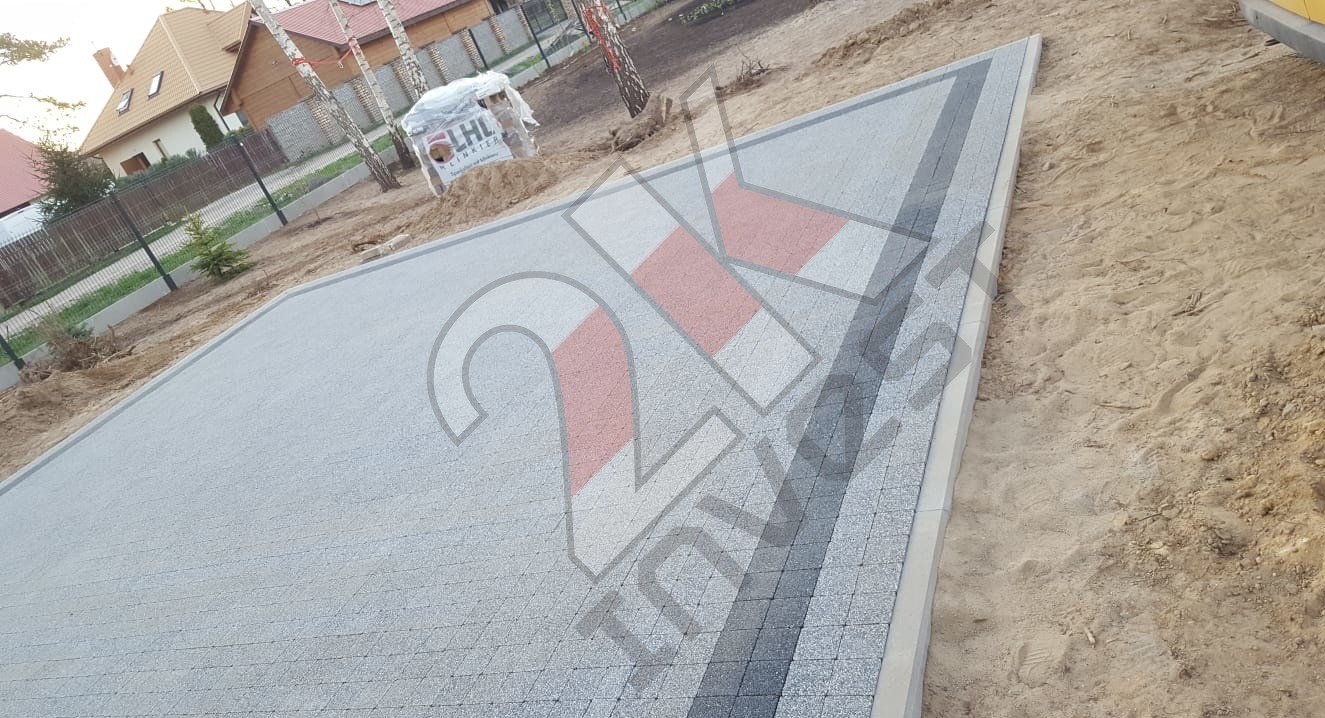 Powierzchnia z jasnoszarej kostki granitowej z ciemnoszarym obramowaniem, widoczny worek z kostką w tle, teren przygotowany pod dalsze prace.