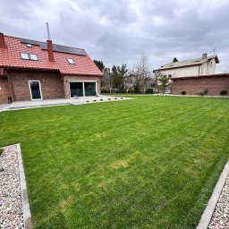 A-Z Ogród Damian Mroch - Perfekcyjnie skoszony trawnik przed nowoczesnym domem z czerwoną dachówką i panelami słonecznymi. Widoczny kamienny chodnik i ozdobne nasadzenia.