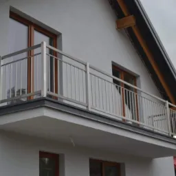 Balkon z nowoczesną, metalową balustradą o minimalistycznym designie, widok z dołu, szara elewacja budynku z drewnianymi ramami okiennymi.