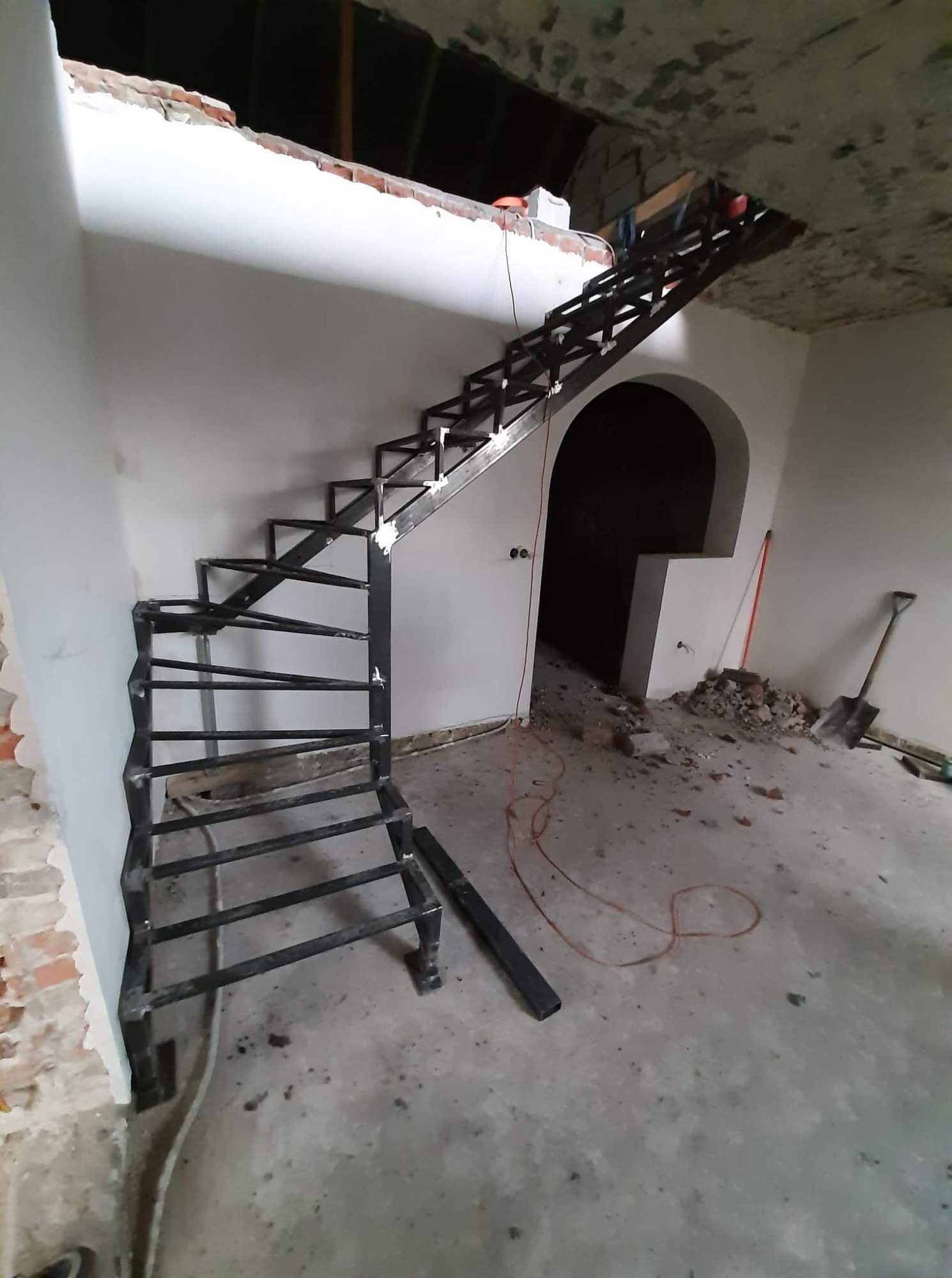 Surowe, niedokończone, metalowe schody o konstrukcji kratownicowej, zamontowane w surowym stanie wewnątrz budynku w trakcie remontu, widoczne ślady gruzu i narzędzia.