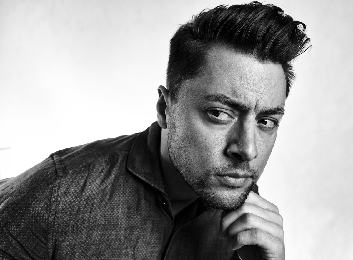 Czarno-biały portret mężczyzny z zaczesanymi włosami, opierającego brodę na dłoni i spoglądającego w bok z wyrazistym spojrzeniem.