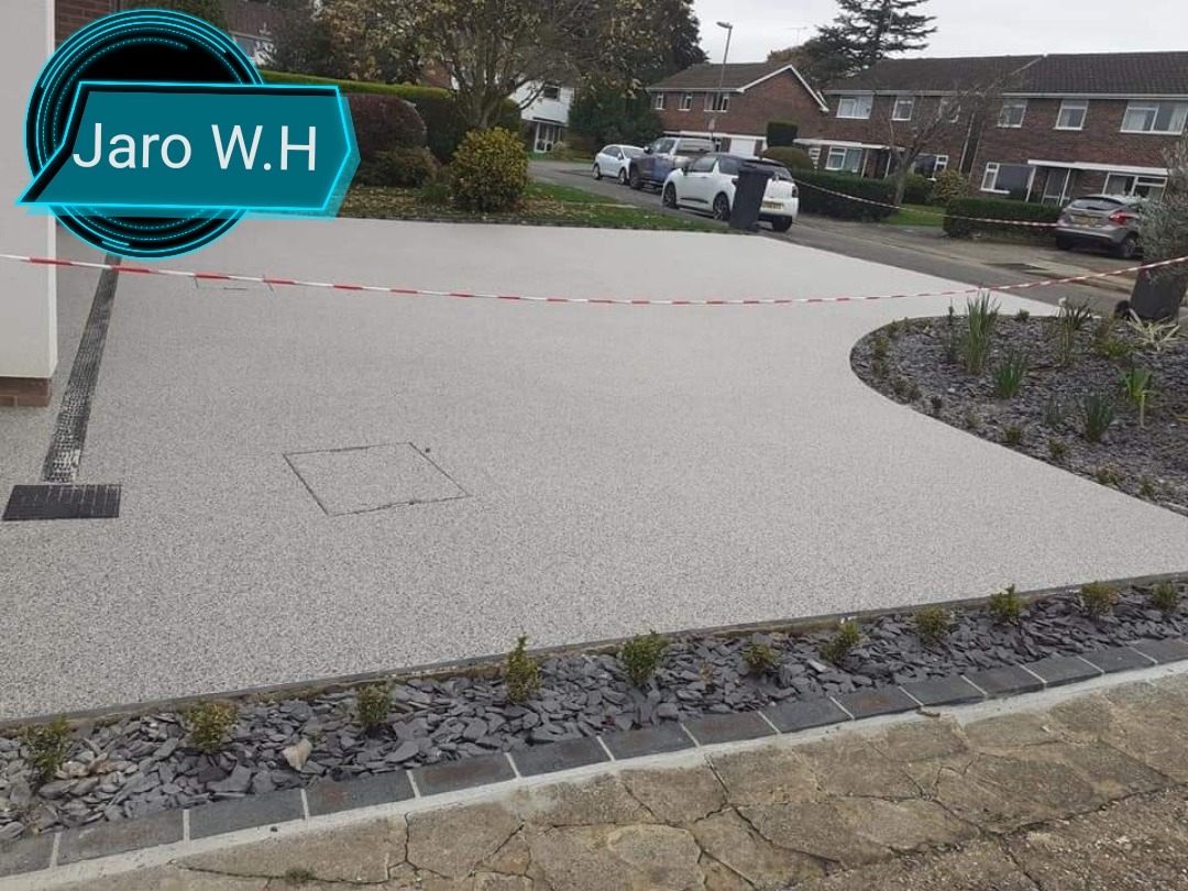 Żywiczna nawierzchnia podjazdu do domu, z odpływem liniowym i studzienką rewizyjną, obrzeże z łupka i kostki, częściowo zabezpieczona taśmą ostrzegawczą.