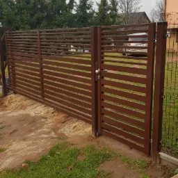 Nowoczesna, pozioma brama przesuwna z brązowych paneli, z widocznym zamkiem i słupkami, na tle domu i zieleni.