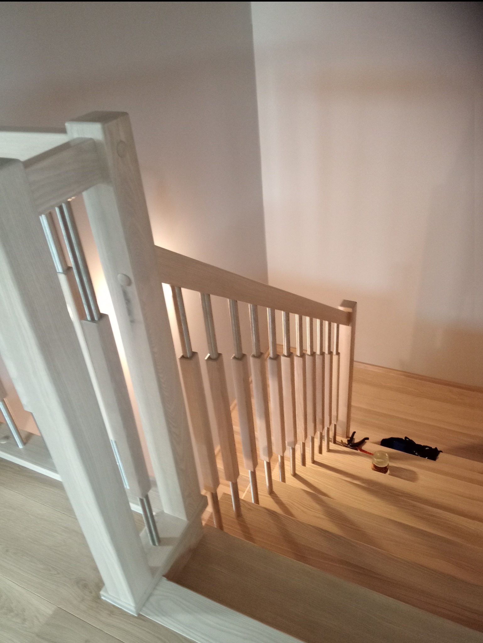 Jasne drewniane schody z metalowymi balustradami, widok z góry, na jednym ze stopni leżą narzędzia i akcesoria montażowe.