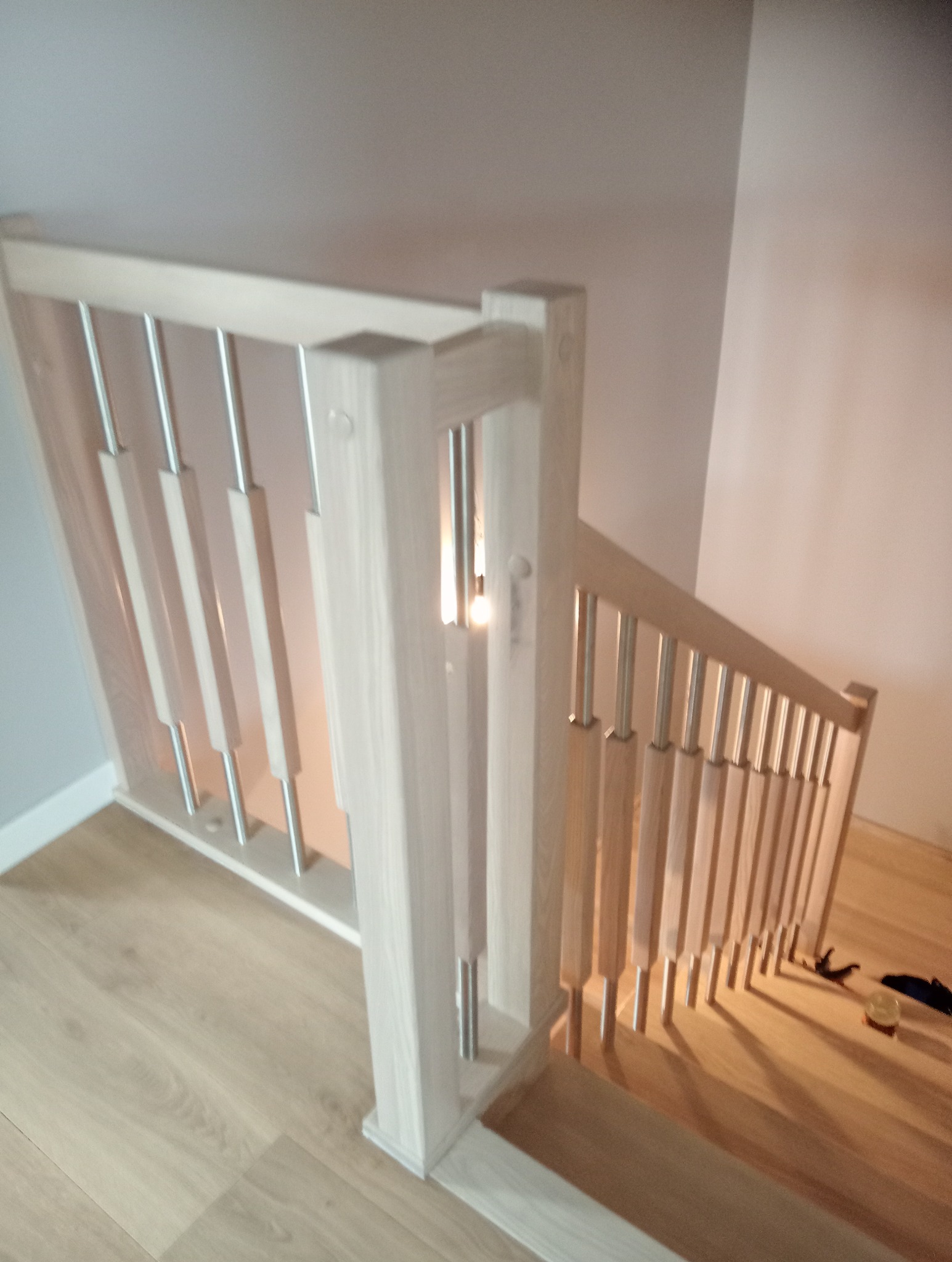 Jasne schody z drewnianą balustradą i metalowymi elementami, widok z góry na podest, z widocznymi drobnymi narzędziami lub elementami montażowymi na stopniach.