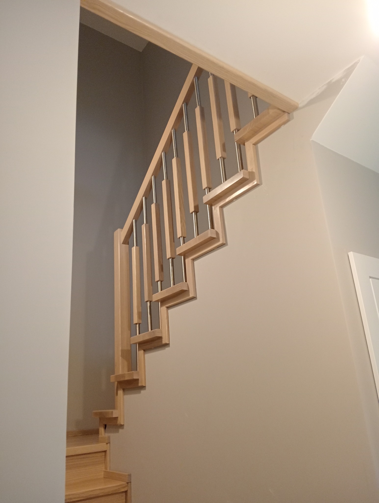 Jasne drewniane schody z metalowymi balustradami, widok z dołu, neutralne tło ścian
