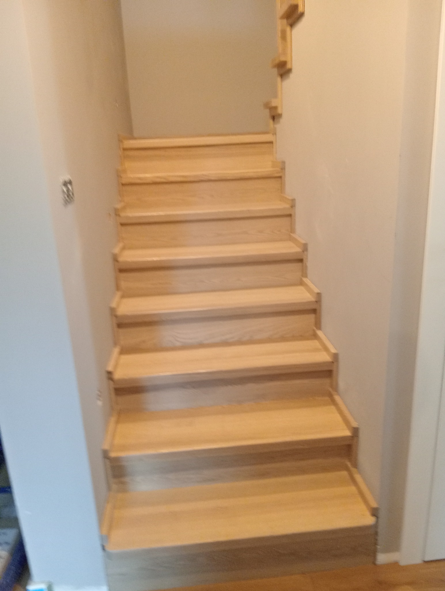 Jasne, proste schody z drewna prowadzące w górę, widoczne z dołu, z minimalistyczną balustradą przy ścianie.