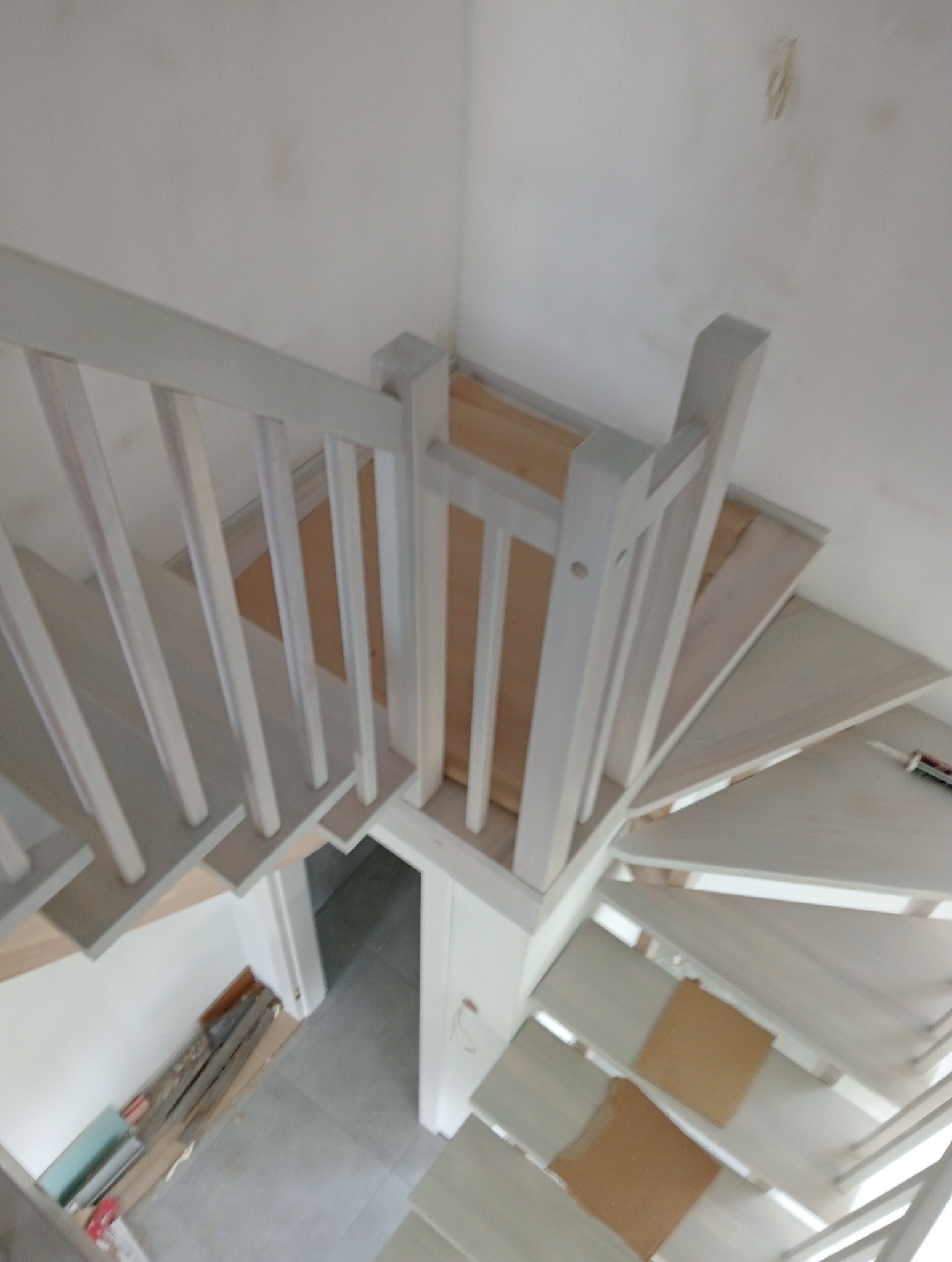 Widok z góry na spiralne, drewniane schody z białymi balustradami w Bolewicach, z widocznymi niedoskonałościami wykończenia i elementami zabezpieczającymi stopnie.