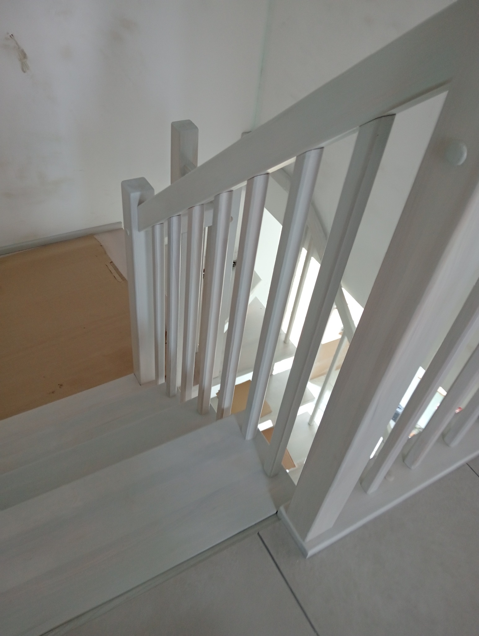 Białe, drewniane schody z balustradą, widok z góry, jasne wnętrze, fragment podłogi wyłożonej płytkami.