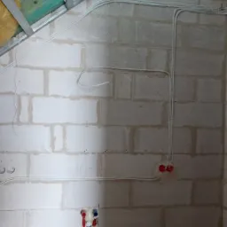 Białe przewody elektryczne ułożone na surowej ścianie z betonu komórkowego, widoczne puszki instalacyjne i fragment konstrukcji sufitu podwieszanego.