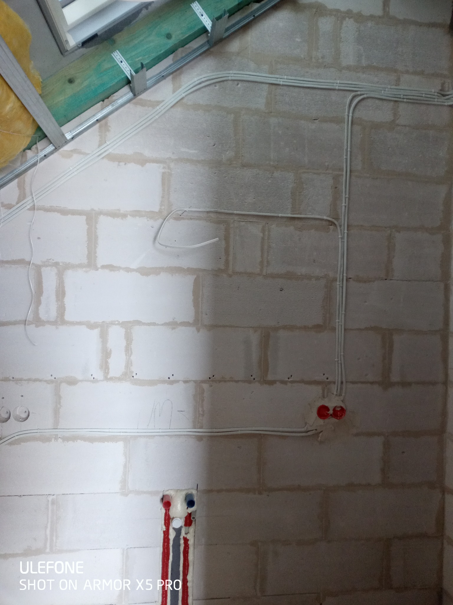 Białe przewody elektryczne ułożone na surowej ścianie z betonu komórkowego, widoczne puszki instalacyjne i fragment konstrukcji sufitu podwieszanego.