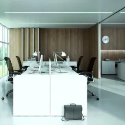 Nowoczesne biuro z białymi biurkami, ergonomiczne krzesła, drewniane panele ścienne i betonowa ściana z dużym zdjęciem, uzupełnione roślinami w czarnych donicach i aktówką leżącą pod biurkiem.