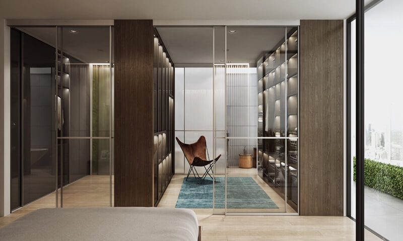 Przestronna garderoba z przesuwnymi szklanymi drzwiami, oświetleniem LED wewnątrz szaf i fotelem typu motyl na turkusowym dywanie.