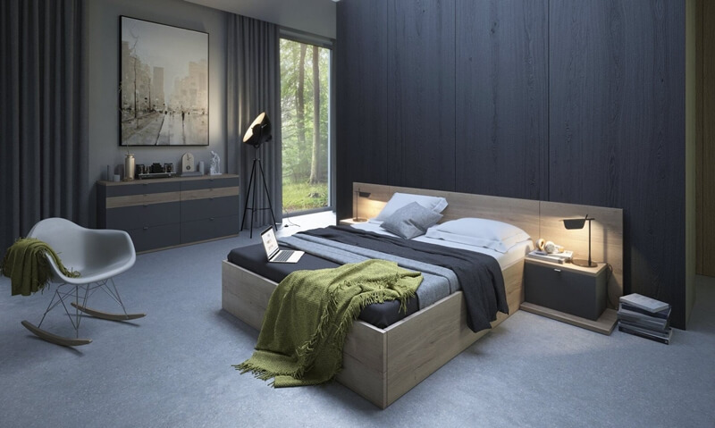 Nowoczesna sypialnia z łóżkiem z drewnianą ramą, szarą pościelą i narzutą w odcieniu oliwkowym. W tle komoda z szufladami, lampa studyjna na trójnogu i obraz z motywem miejskim.