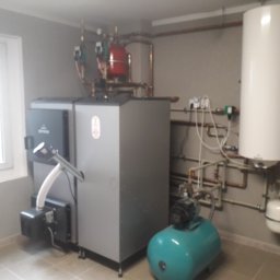 Instalacje Sanitarne Michał Szczepaniak - Kompletna kotłownia z kotłem na paliwo stałe, zasobnikiem ciepłej wody i instalacją hydrauliczną w pomieszczeniu z oknem.
