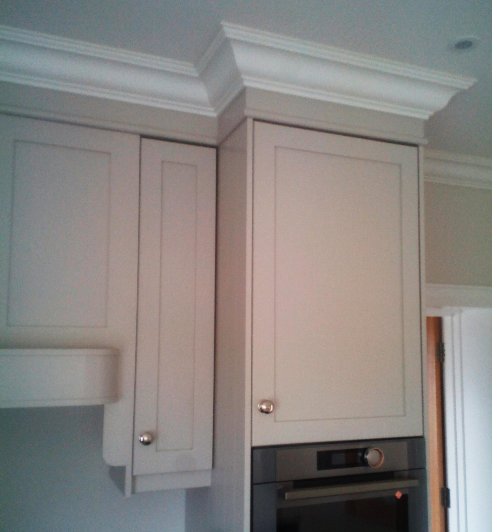 Jasne szafki kuchenne z ozdobnym frezowaniem pod sufitem, zabudowane z piekarnikiem.