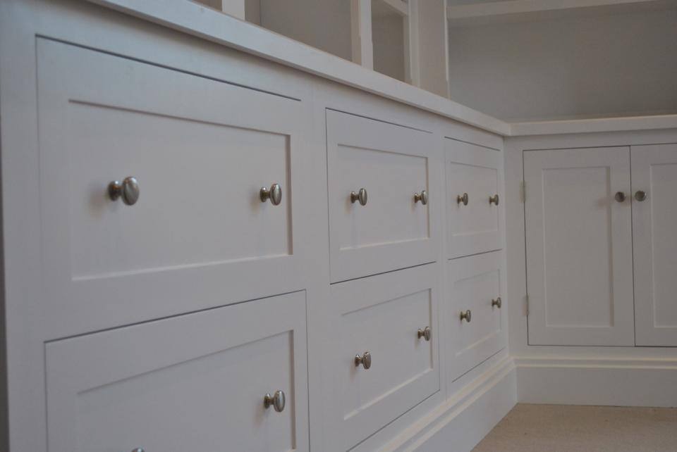 Biała zabudowa meblowa z szufladami i szafkami, z metalowymi gałkami, wbudowana w ścianę.