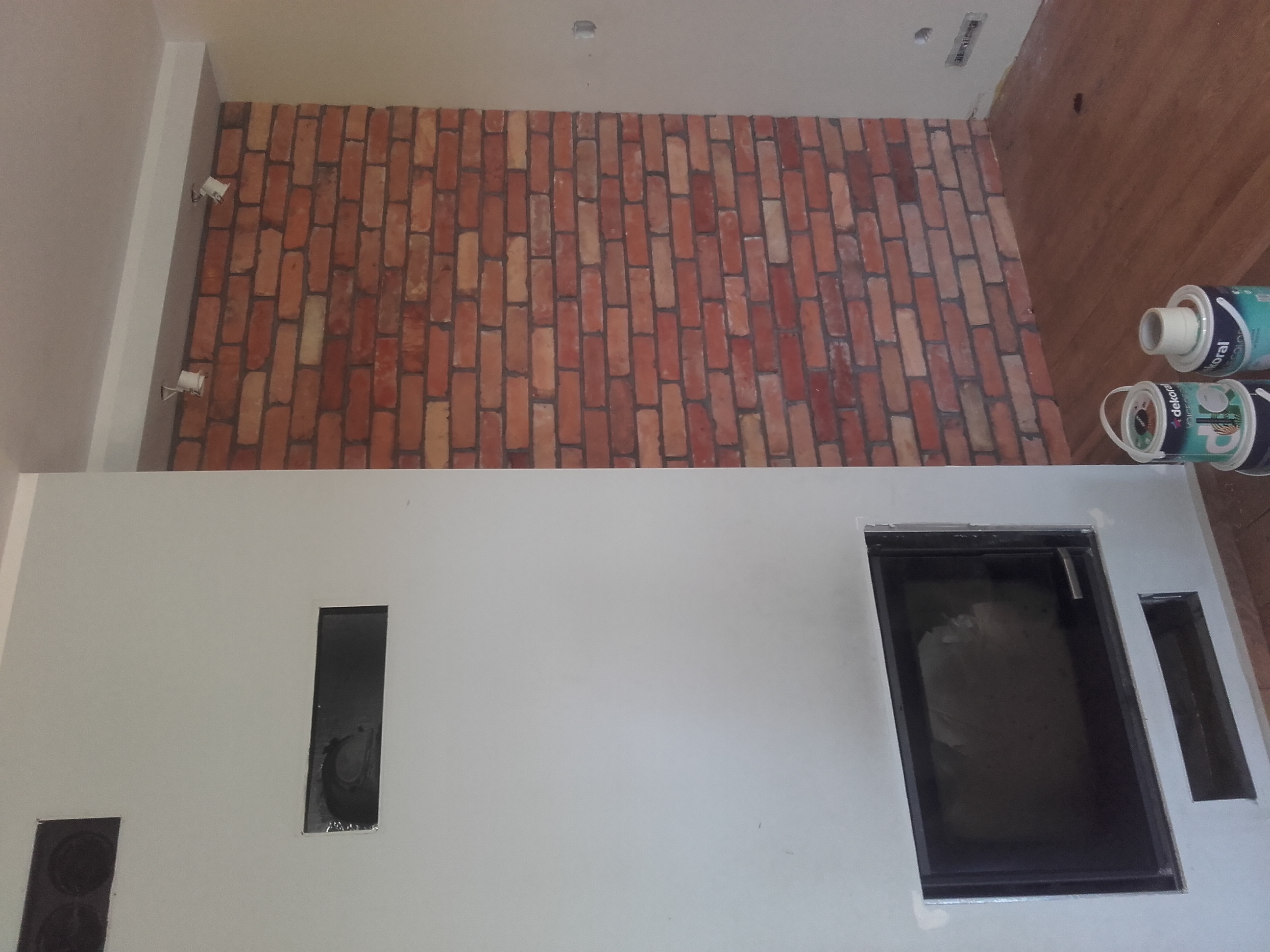 Ściana wykończona czerwoną cegłą, pomalowana ściana z wnękami, widoczne puszki farby.