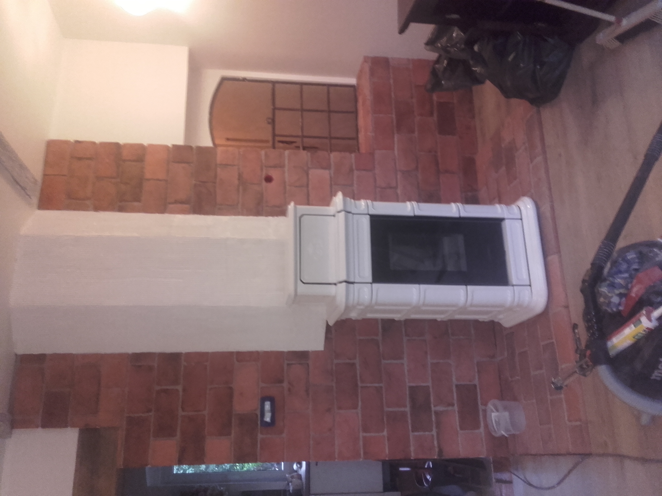 Wykończony kominek z białym obramowaniem i ceglaną obudową, widoczne narzędzia pracy i resztki materiałów.