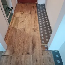 Układanie paneli podłogowych w korytarzu, widoczna część ułożonej podłogi z paneli drewnopodobnych oraz podkład pod panele przy ścianie. Uwagę zwraca wzór i kolor paneli.