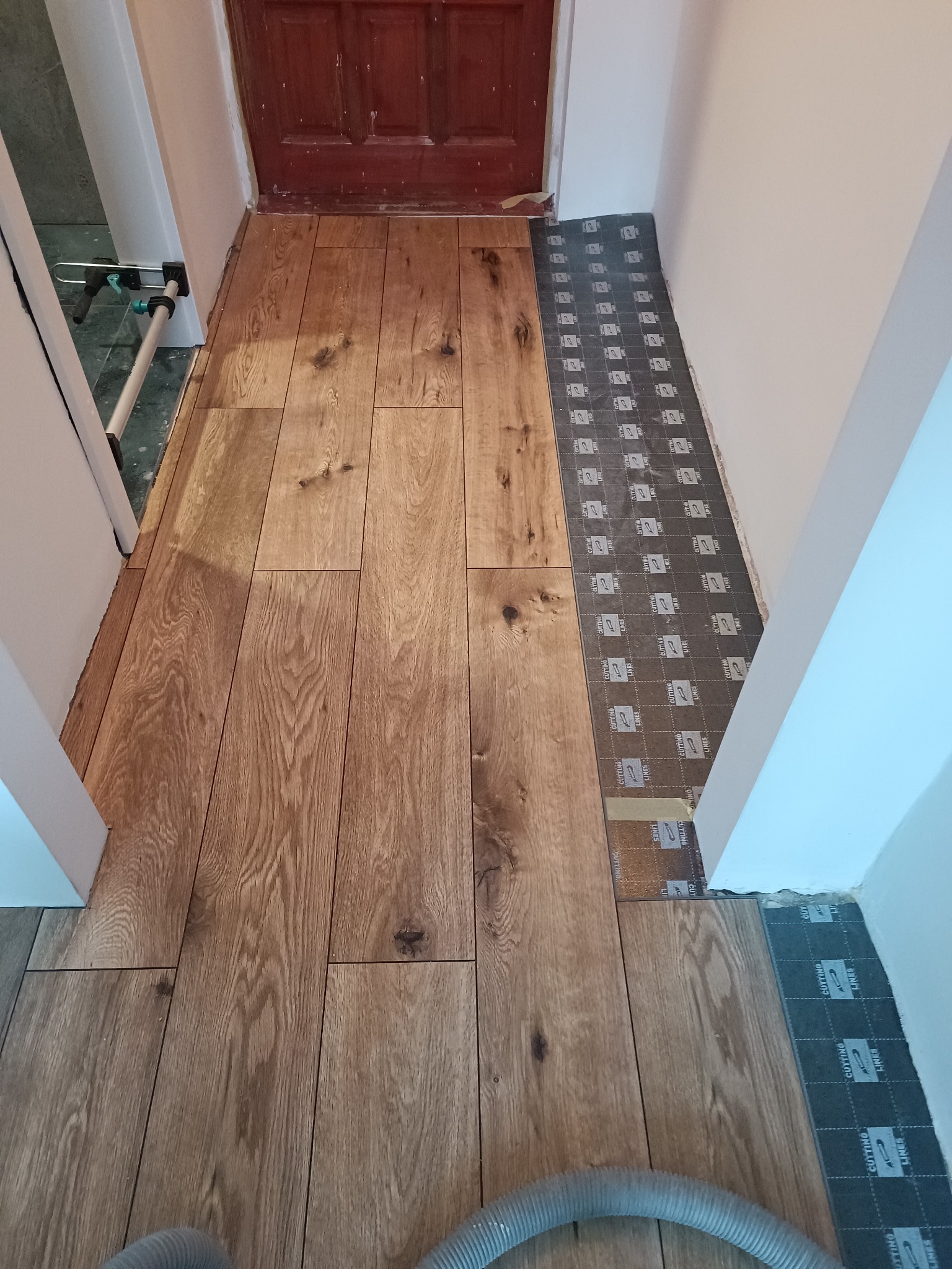 Układanie paneli podłogowych w korytarzu, widoczna część ułożonej podłogi z paneli drewnopodobnych oraz podkład pod panele przy ścianie. Uwagę zwraca wzór i kolor paneli.