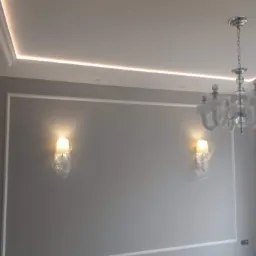 Szara ściana z białymi listwami dekoracyjnymi, podświetlany sufit, kinkietami zabezpieczonymi folią i żyrandolem owiniętym w folię ochronną podczas prac wykończeniowych.