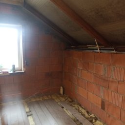 NIKO - Poddasze w trakcie prac: widoczne ocieplenie między legarami podłogi, ceglana ściana z laserowym poziomowaniem i skośny sufit z izolacją. Okno w tle.