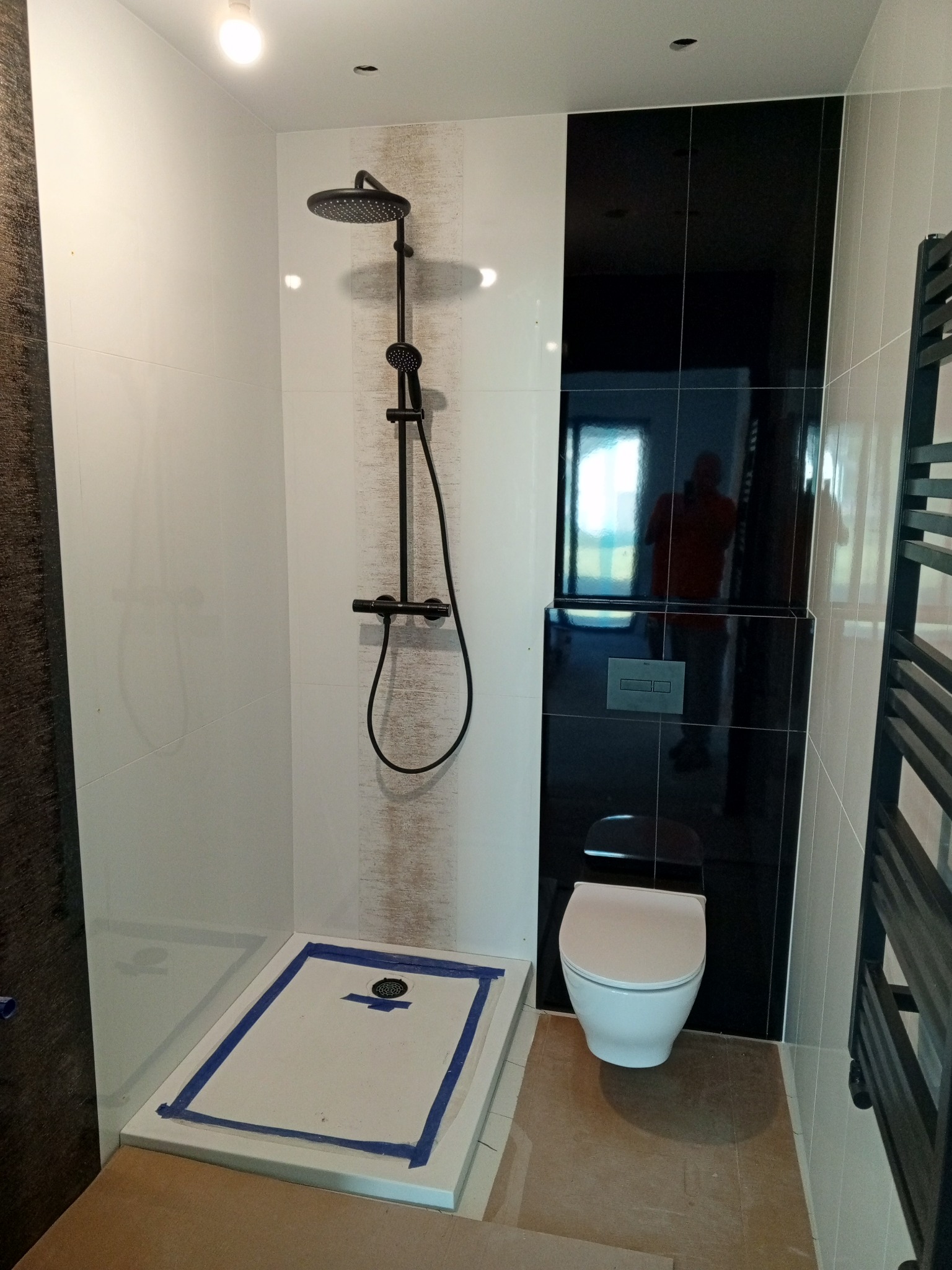 Nowoczesna łazienka z czarną armaturą: deszczownica, toaleta podwieszana na tle czarnych płytek. Uwagę zwraca kontrast bieli i czerni oraz minimalistyczny design.