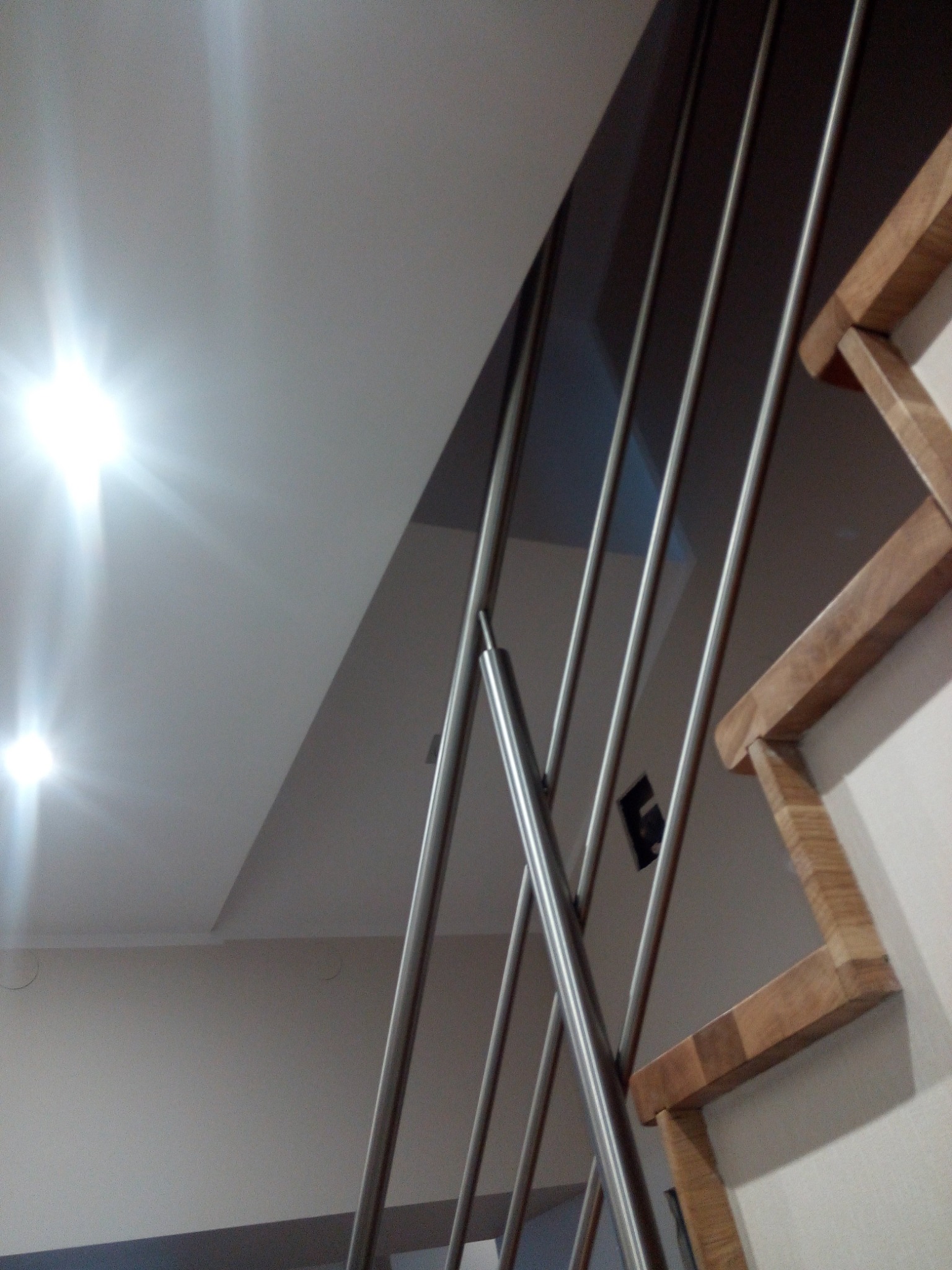 Nowoczesne schody z drewnianymi stopniami i metalowymi balustradami, widok z dołu na jasny sufit z oświetleniem punktowym.