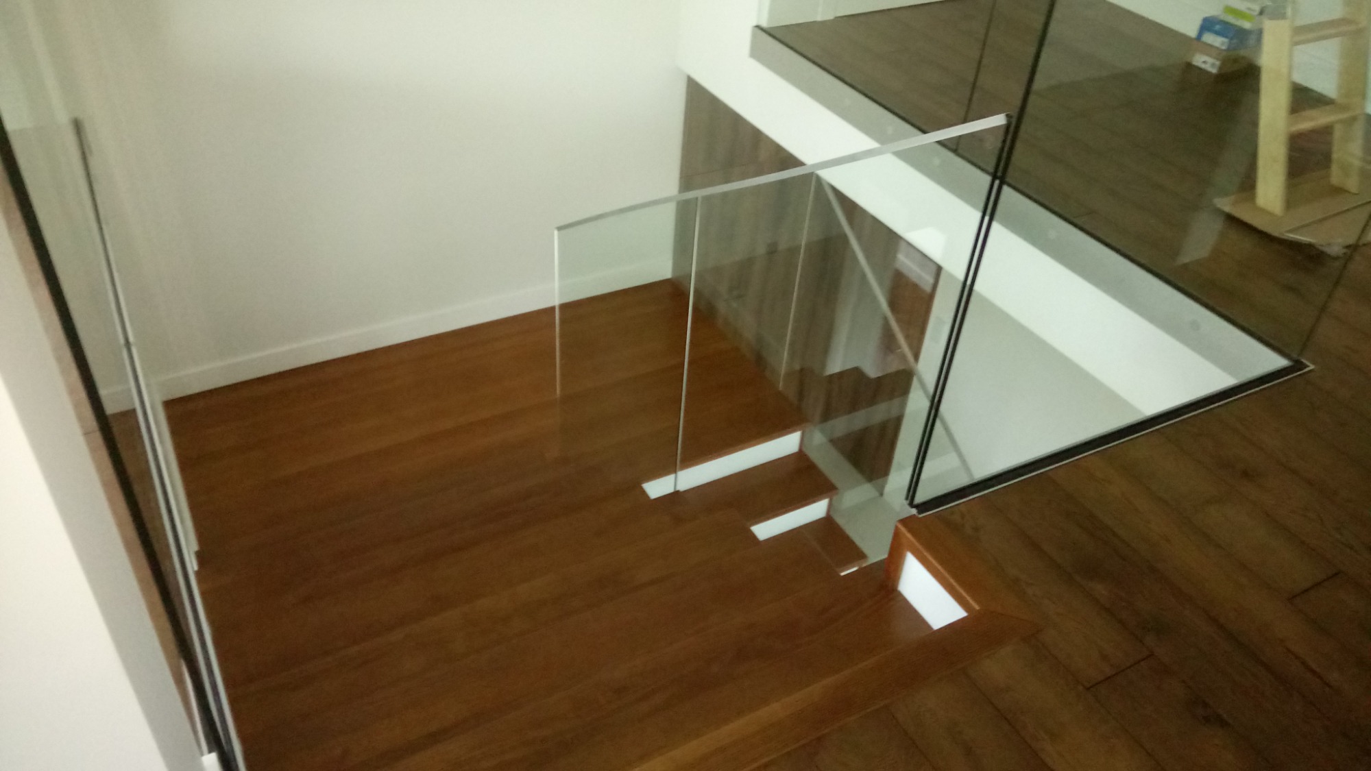 Nowoczesne schody z drewna egzotycznego z balustradą ze szkła hartowanego, widok z góry na pierwsze stopnie.