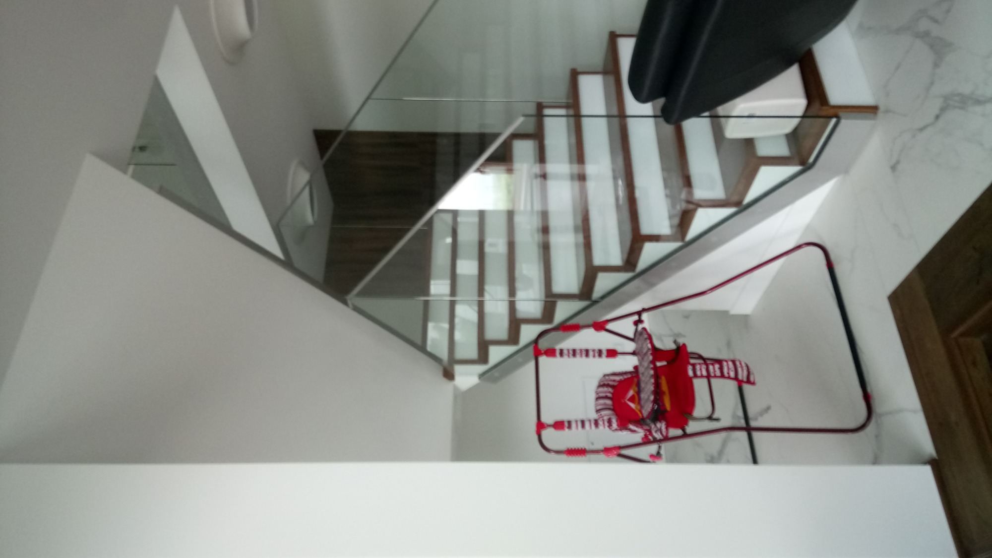 Nowoczesne schody z drewnianymi stopniami i szklaną balustradą w domu w Łagowie, widziane z góry, z fragmentem dziecięcej huśtawki w dolnej części kadru.