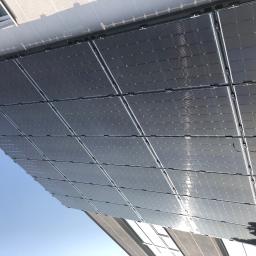 Marit - Instalacja fotowoltaiczna na dachu budynku, widok od dołu pod kątem, panele w czarnych ramach odbijają błękitne niebo.