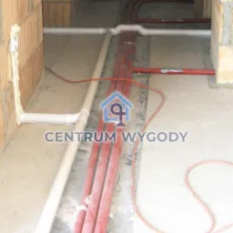Instalacja rur w bruzdach w ścianie, widoczne rury białe i czerwone, fragment ściany z pustaków ceramicznych. Na zdjęciu widoczny znak wodny.