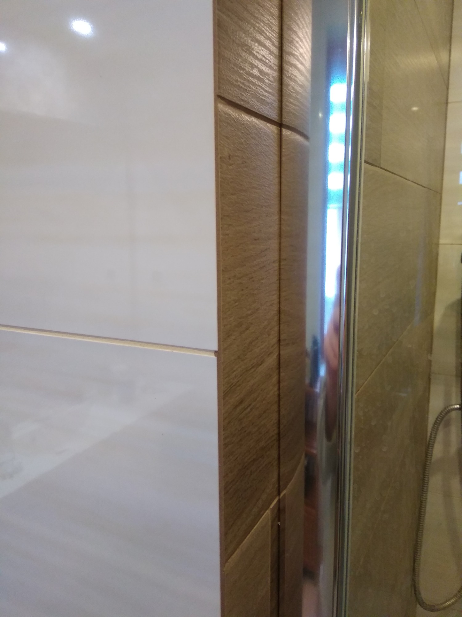 Fragment łazienki z widocznymi płytkami w odcieniach bieli i brązu, oraz fragment kabiny prysznicowej z chromowanymi elementami.