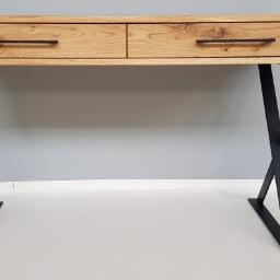 Montex - Biurko z blatem z jasnego drewna z widocznymi słojami i dwoma szufladami z czarnymi, minimalistycznymi uchwytami, osadzone na czarnych, metalowych nogach w kształcie litery X, na tle szarej ściany.