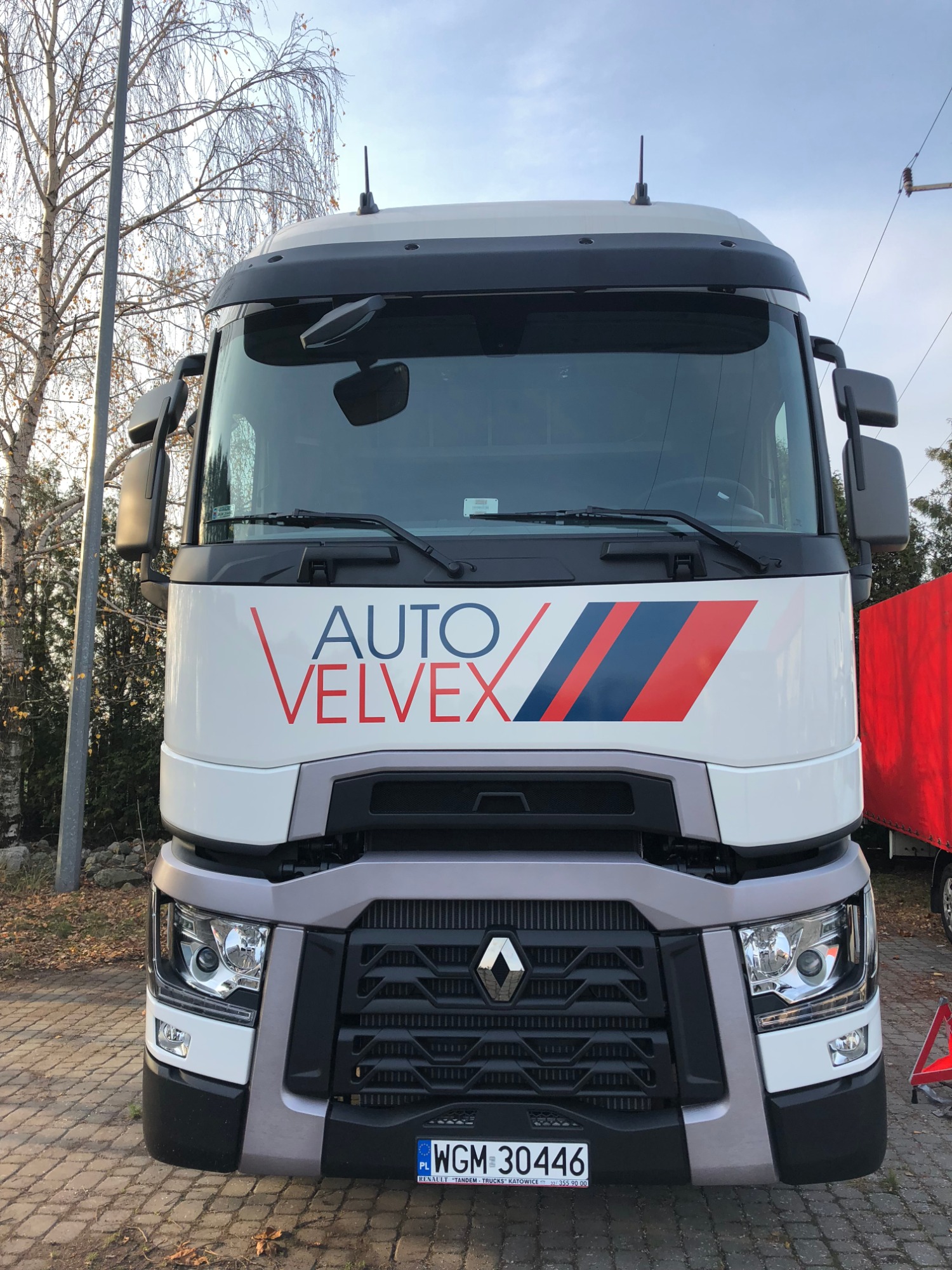 Przód białej ciężarówki Renault z logo firmy Auto Velvex i tablicą rejestracyjną WGM 30446 na brukowanym placu.