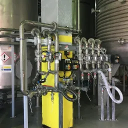 Połączenie rurociągów ze stali nierdzewnej z licznymi zaworami i panelami sterowania, podłączone do dużych zbiorników przemysłowych.